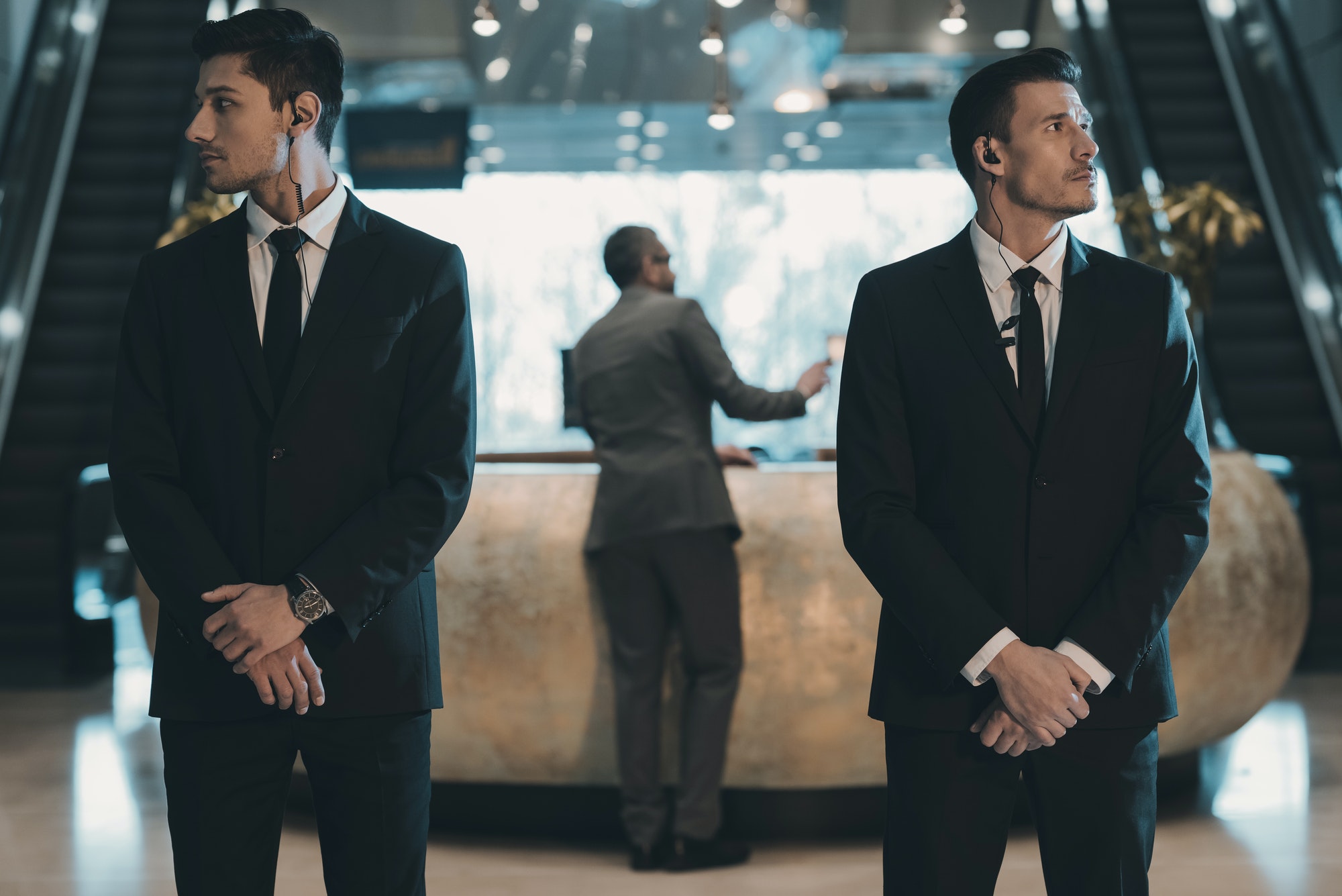 two-bodyguards-waiting-for-businessman-standing-at-reception-counter.jpg